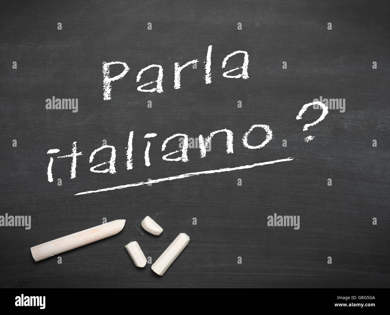 Learning Italian language concept of teacher or student writing parla italiano (do you speak Italian) on blackboard / chalkboard Stock Photo
