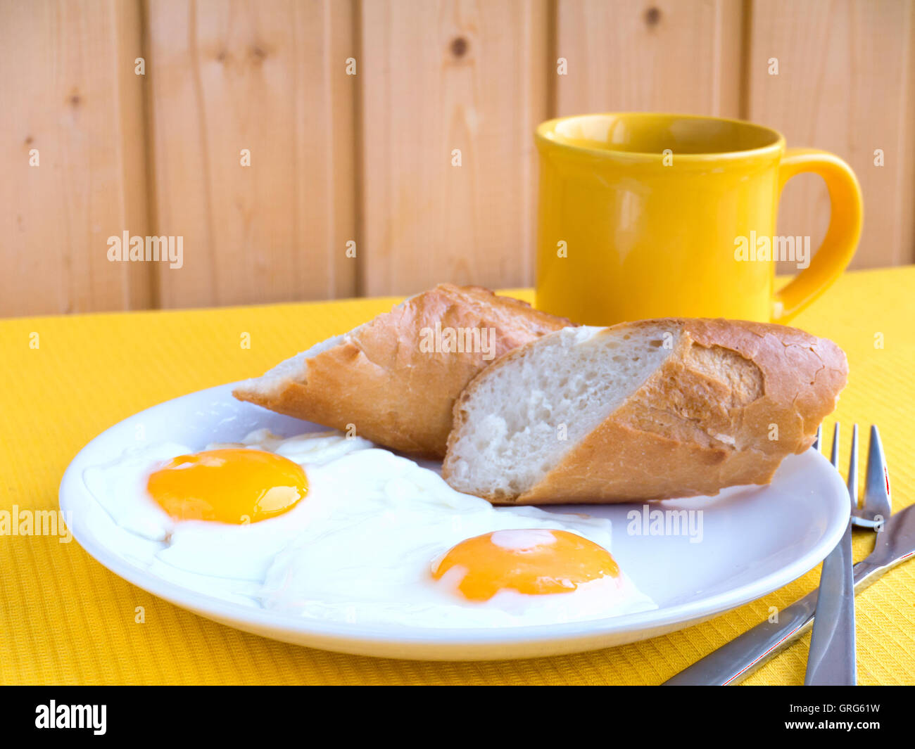 Fried eggs with french baguette slices and coffee americano on the yellow tablecloth Stock Photo