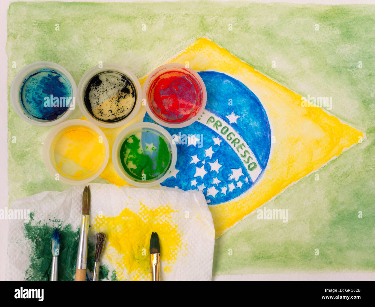 Paints lids, brushes and and stained with paints fabric on the brazil flag watercolor painting Stock Photo