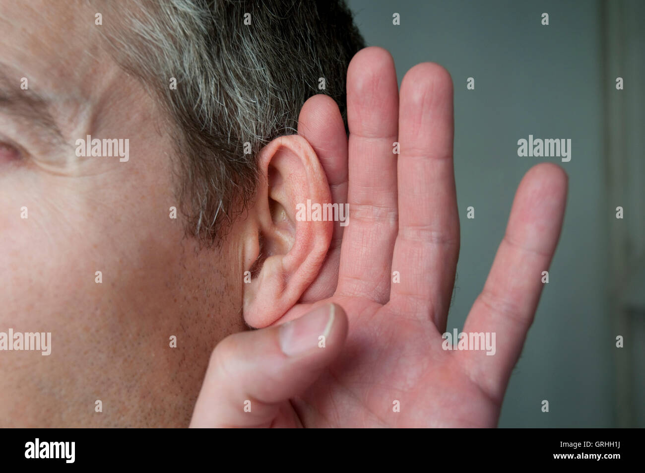 Man's ear with his hand around it to overhear. Close view. Stock Photo