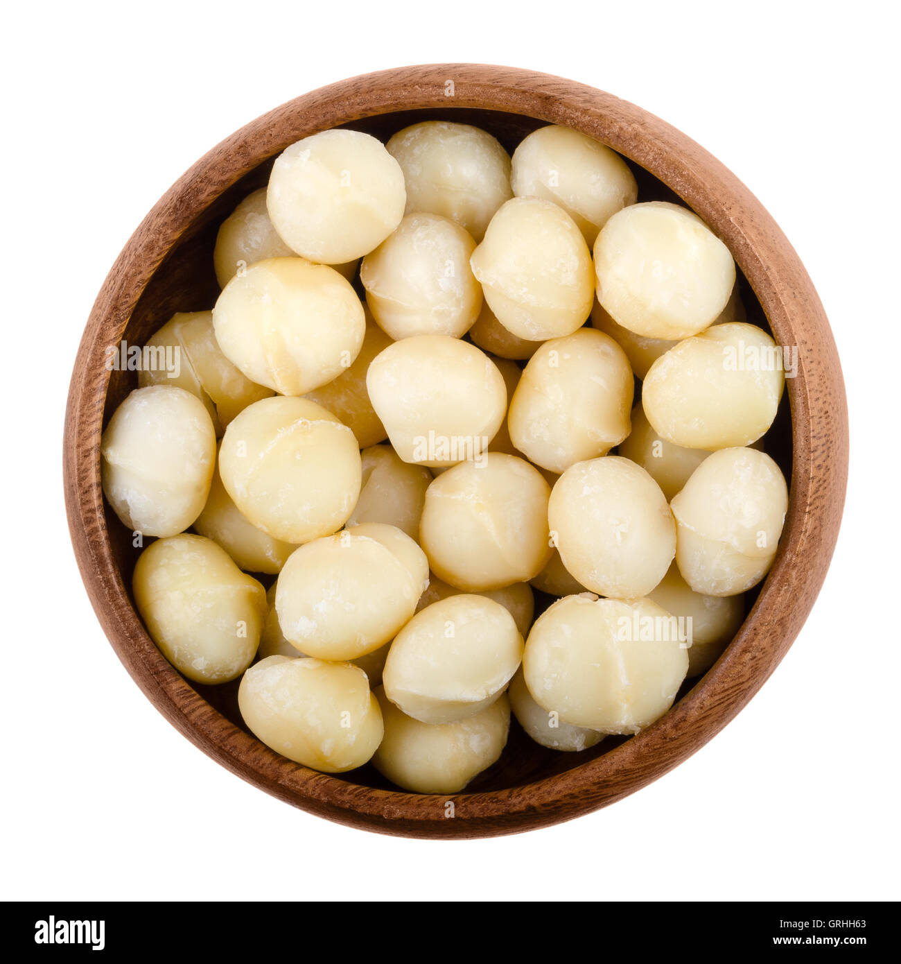 Macadamia nuts in a wooden bowl on white background. Edible seeds without shells. Isolated macro food photo close up from above. Stock Photo