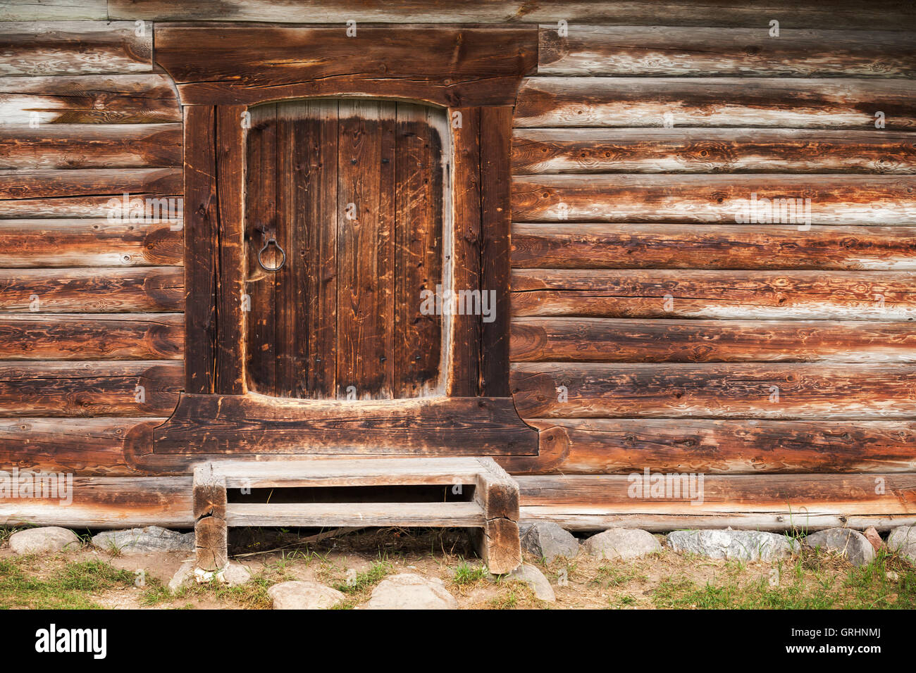 Small closed door in wall made of rough logs. Traditional rural Russian architecture details Stock Photo