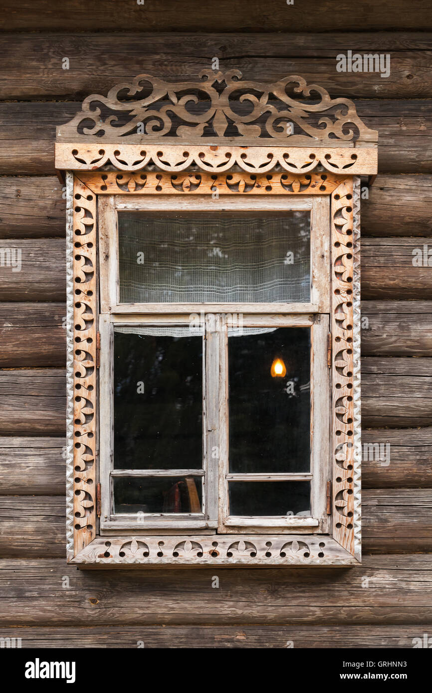 Traditional rural Russian architecture details. Window with carved wooden frame in wall made of rough logs Stock Photo