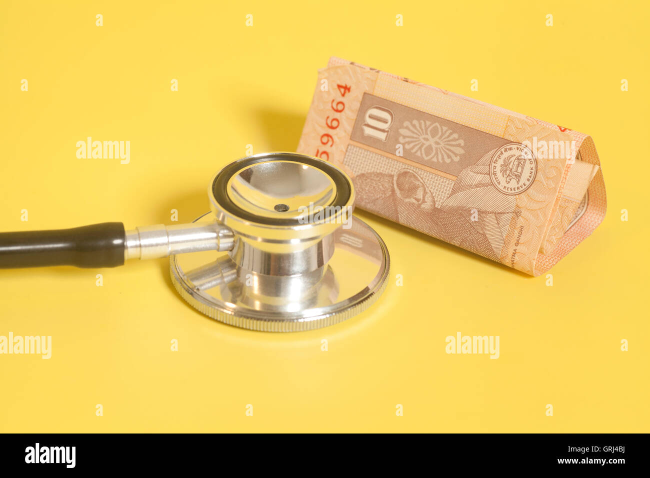 Stethoscope and indian 10 rupee notes on yellow background Stock Photo