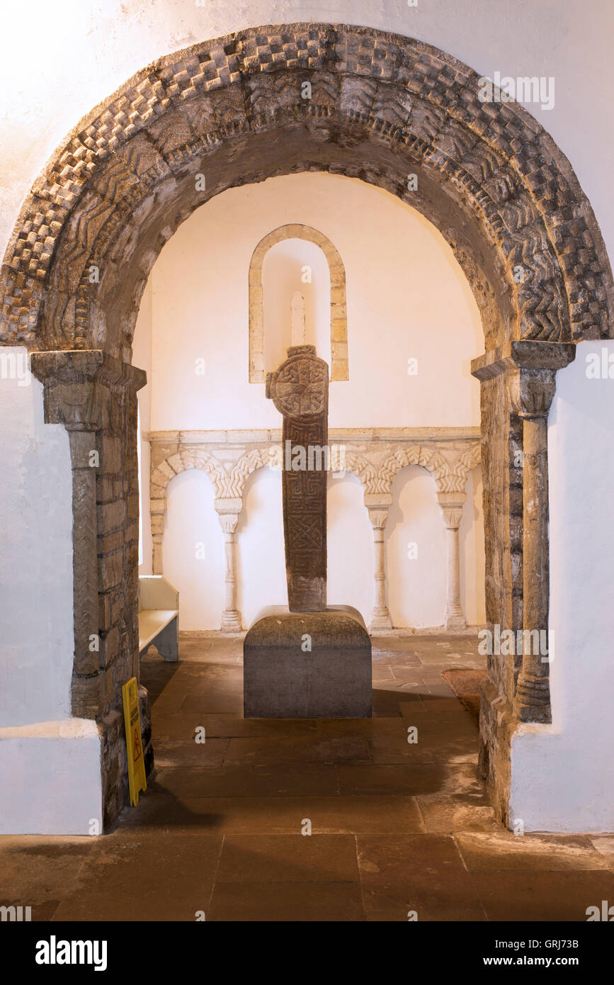 A Norman arch, framing a 10th century cross, in the Priory Church of St. Seiriol, Penmon, Anglesey, Wales, UK Stock Photo