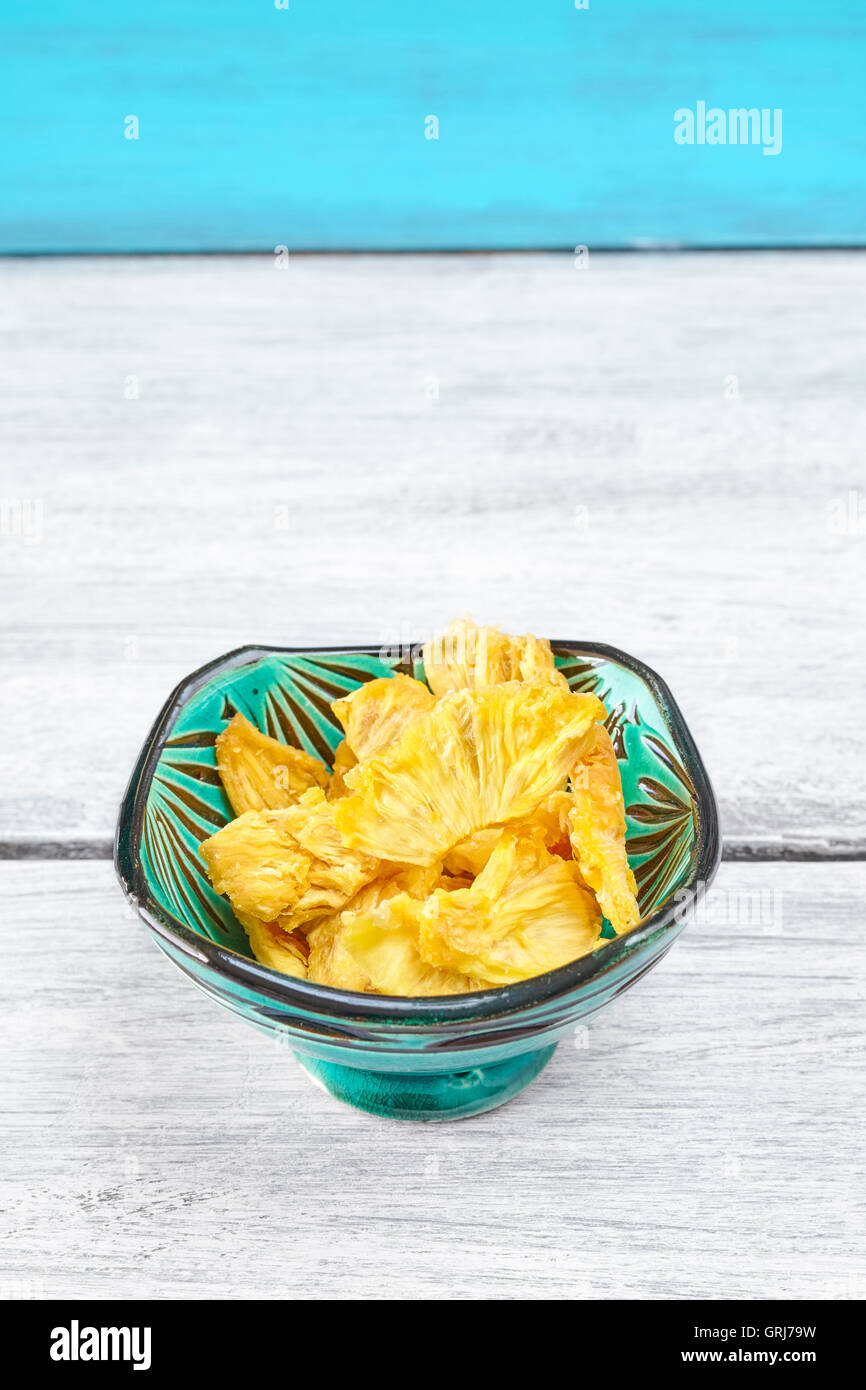 Dried pineapple slices in a green bowl on rustic table, space for text. Stock Photo