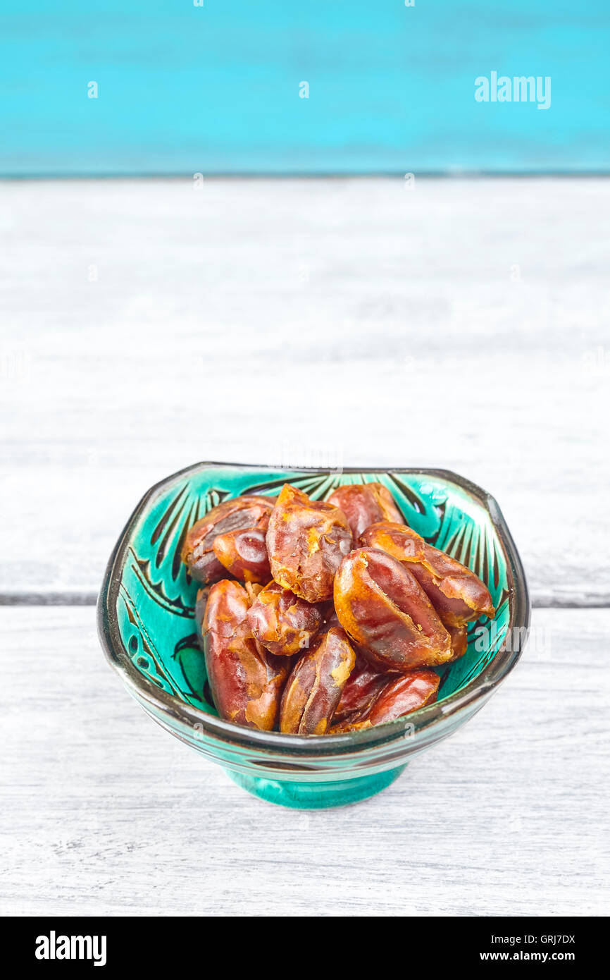 Dried dates in a green bowl on a rustic table, space for text. Stock Photo