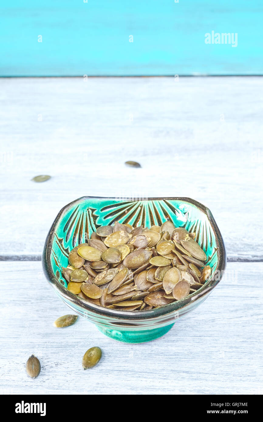 Pumpkin seeds in a green bowl on rustic table, space for text. Stock Photo