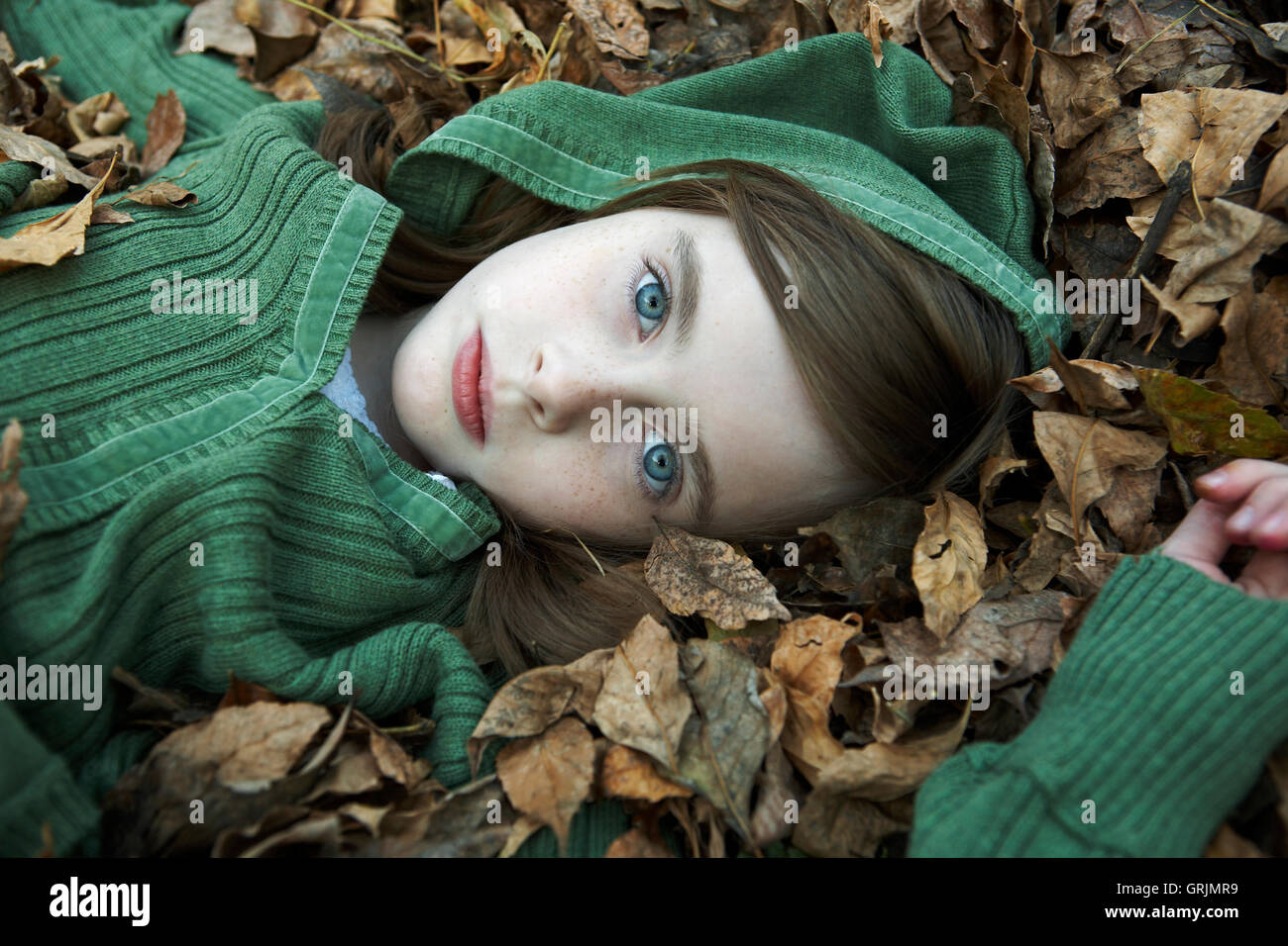portrait of 9 year old girl wearing a hood, lying in autumn leaves. Stock Photo