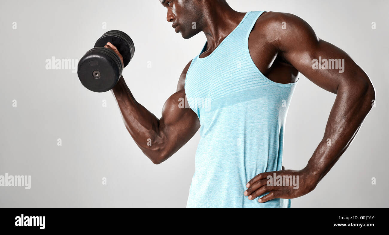 Mixed race man exercising with hand weights against grey background. Young fit man lifting a dumbbell. Stock Photo