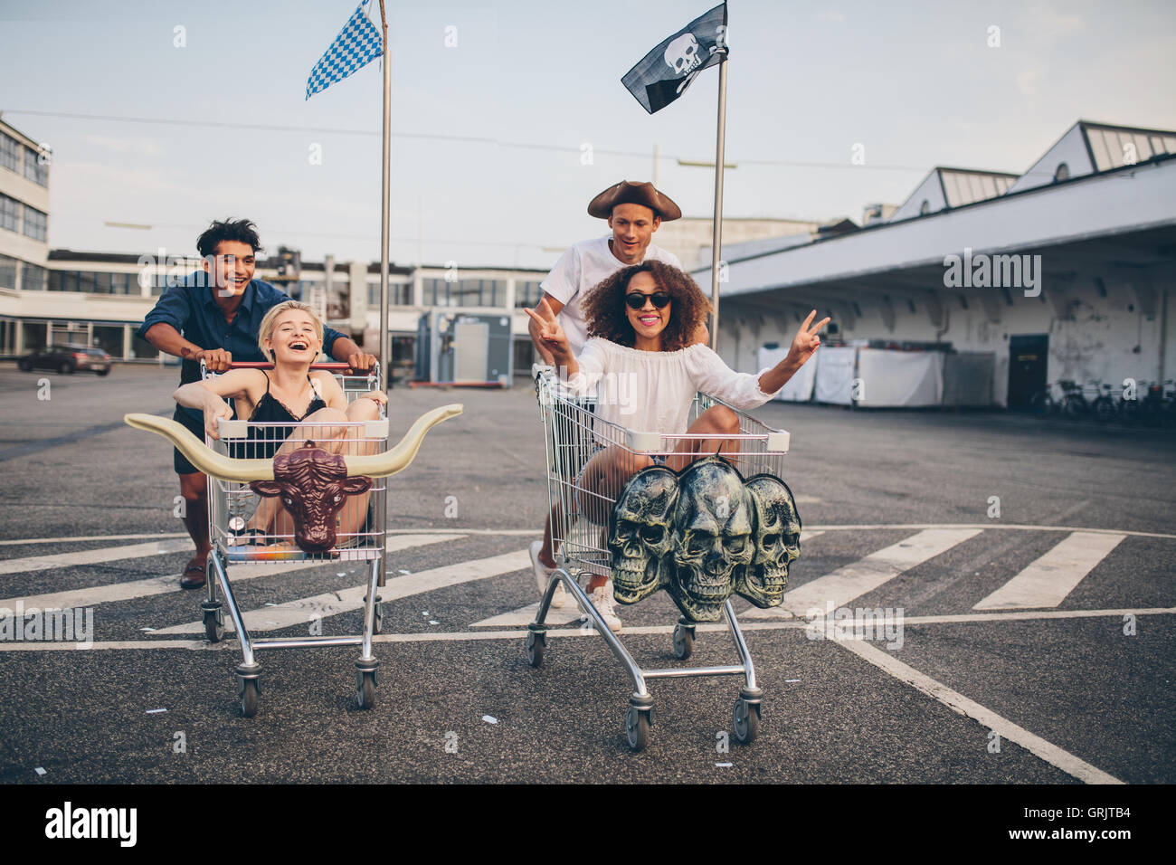 Multiracial group of friends racing with shopping cart. Young people racing with shopping trolleys on road. Stock Photo