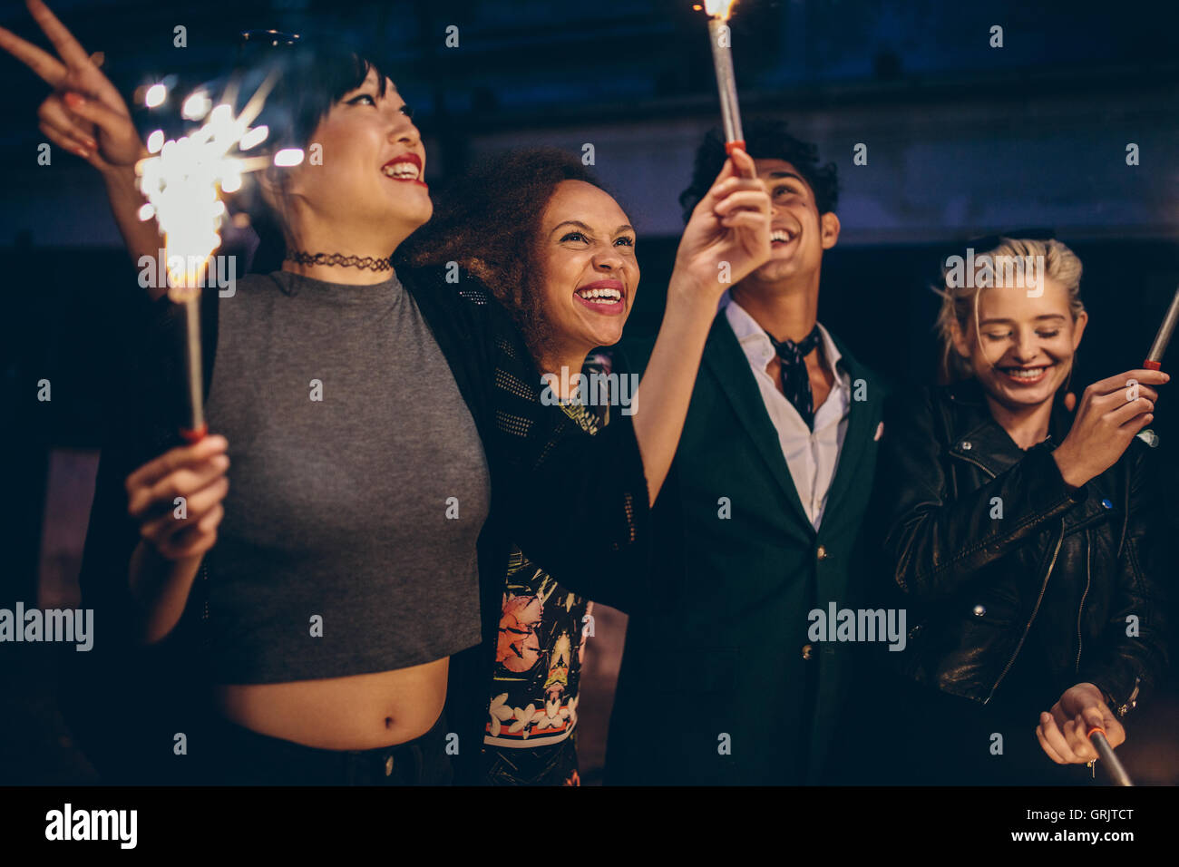 Young friends holding sparklers out on street at night. Group of man and women having night party with sparklers. Stock Photo