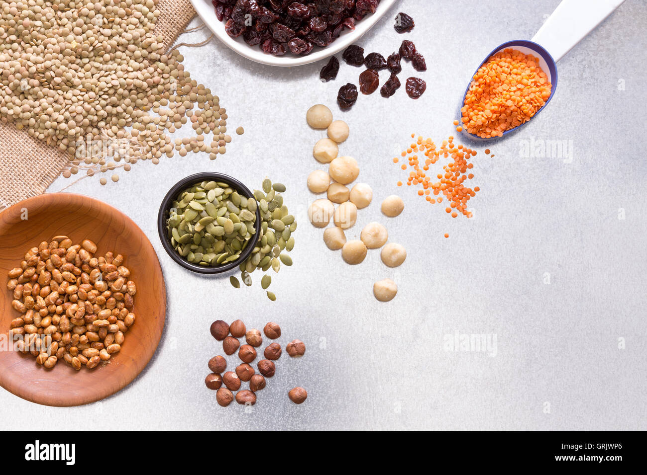 Assorted grains, dried raisins, hazel and macadamia nuts displayed on a white surface for a