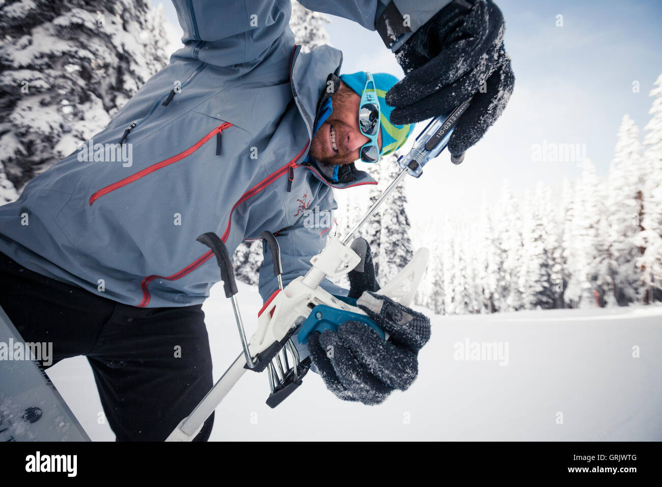A backcountry skier uses a screw driver to set the DIN setting on his binding. Stock Photo