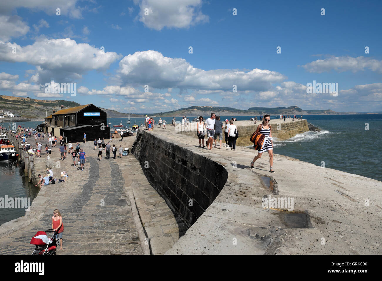 People and woman with striped dress walking on the quay and The Cobb at
