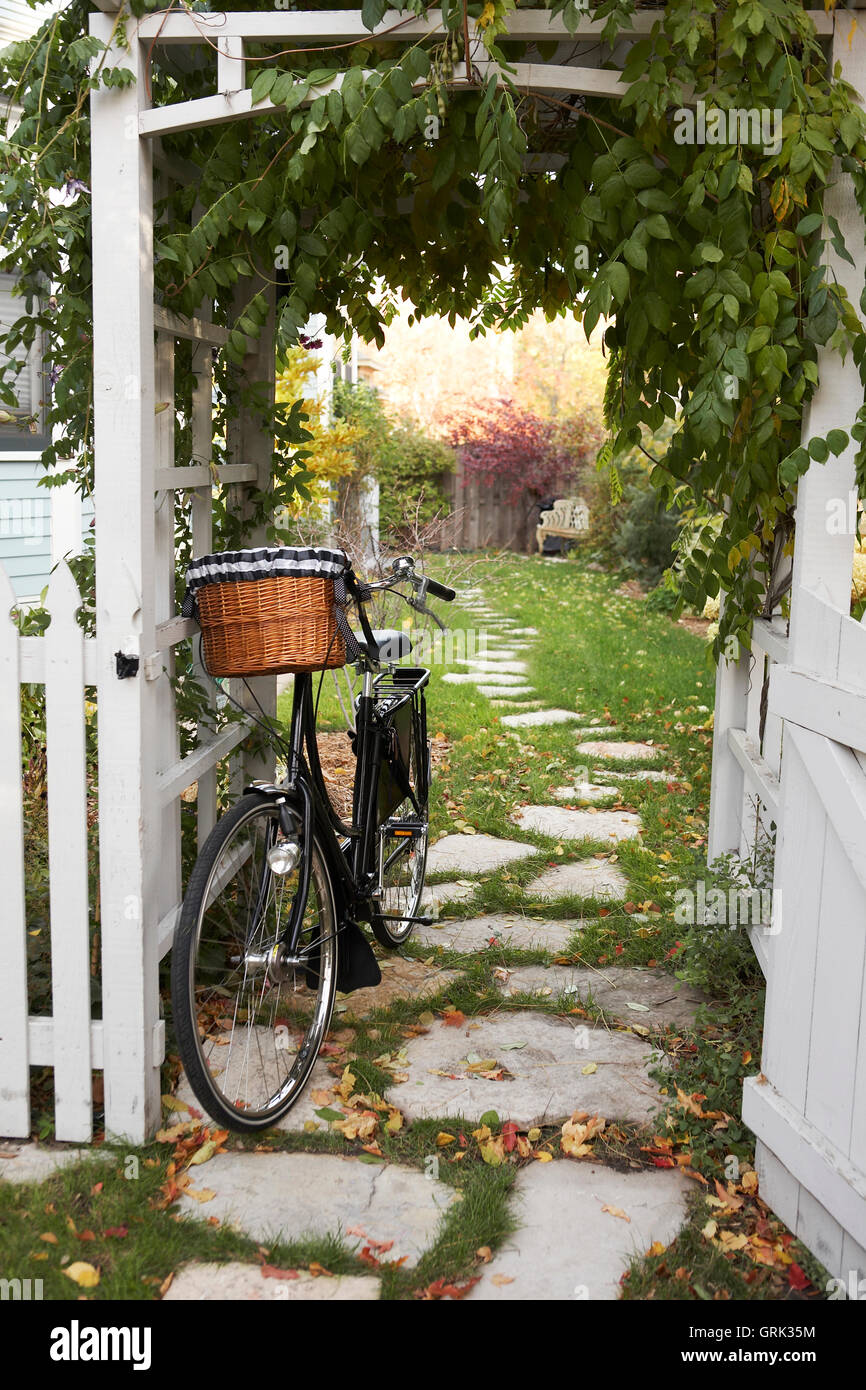 Vintage bicycle with shopping basket leaning against garden arbor trellis Stock Photo