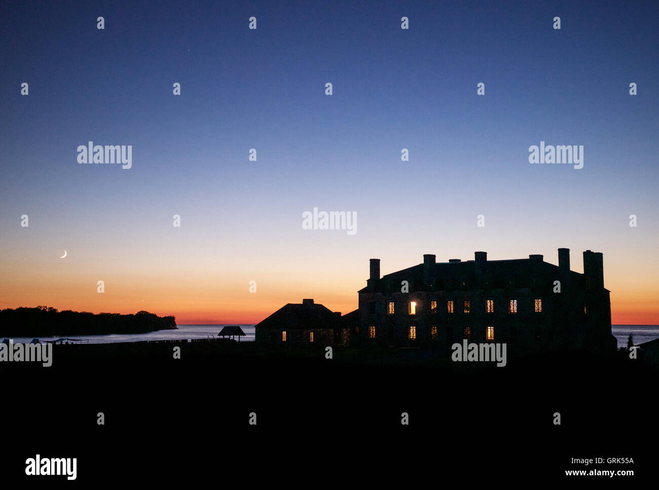View of the 18th-century French chateau at Fort Niagara, New York, at sunset with windows lit up and crescent moon in distance. Stock Photo