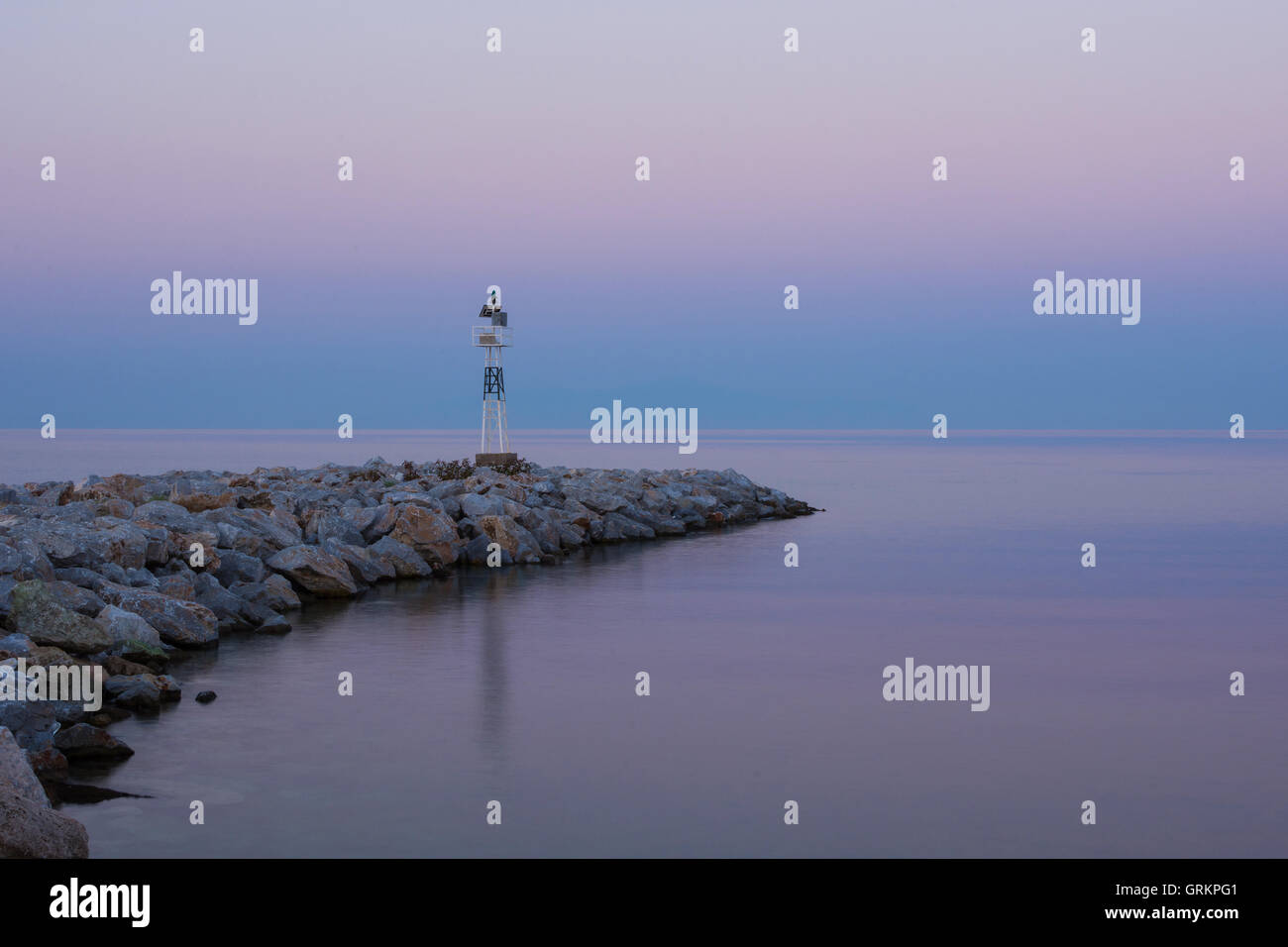 Lighthouse at Sunrise on the Rocky Coast. Dawning and Calm Sea in the Background. Stock Photo