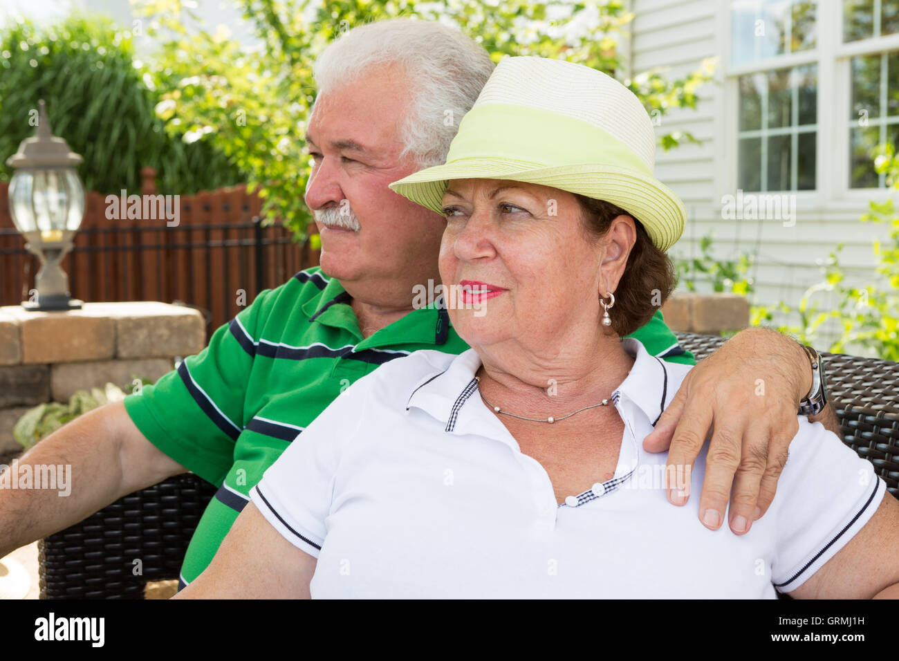 Elderly couple sitting on a wicker settee on an outdoor patio gazing into the distance watching something with serious expressio Stock Photo