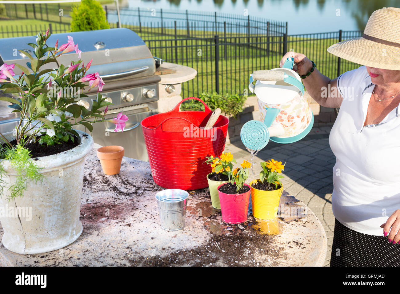 Senior Lady In A Large Sunhat Watering Newly Potted Plants With A