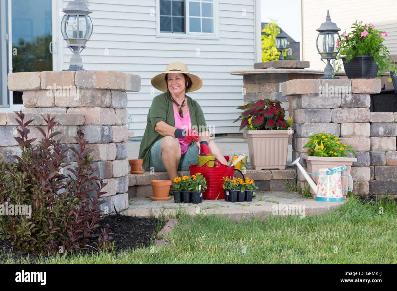 Happy stylish elderly Grandma planting in her garden sitting contentedly on the steps of her porch surrounded by plant seedlings Stock Photo