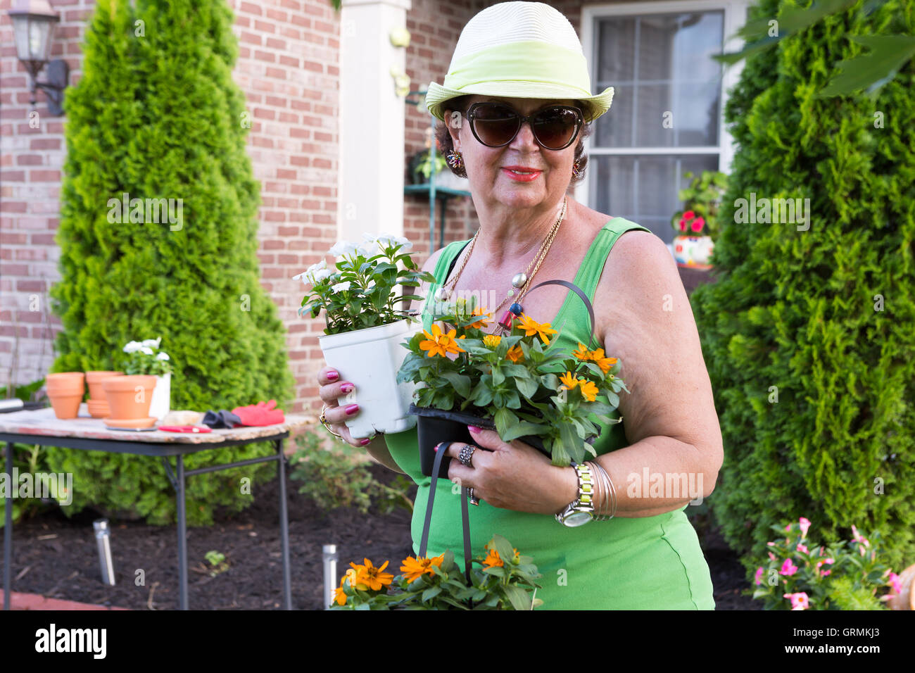 Attractive smiling active senior lady in sunglasses returning from the nursery with colorful ornamental flowering plants and see Stock Photo