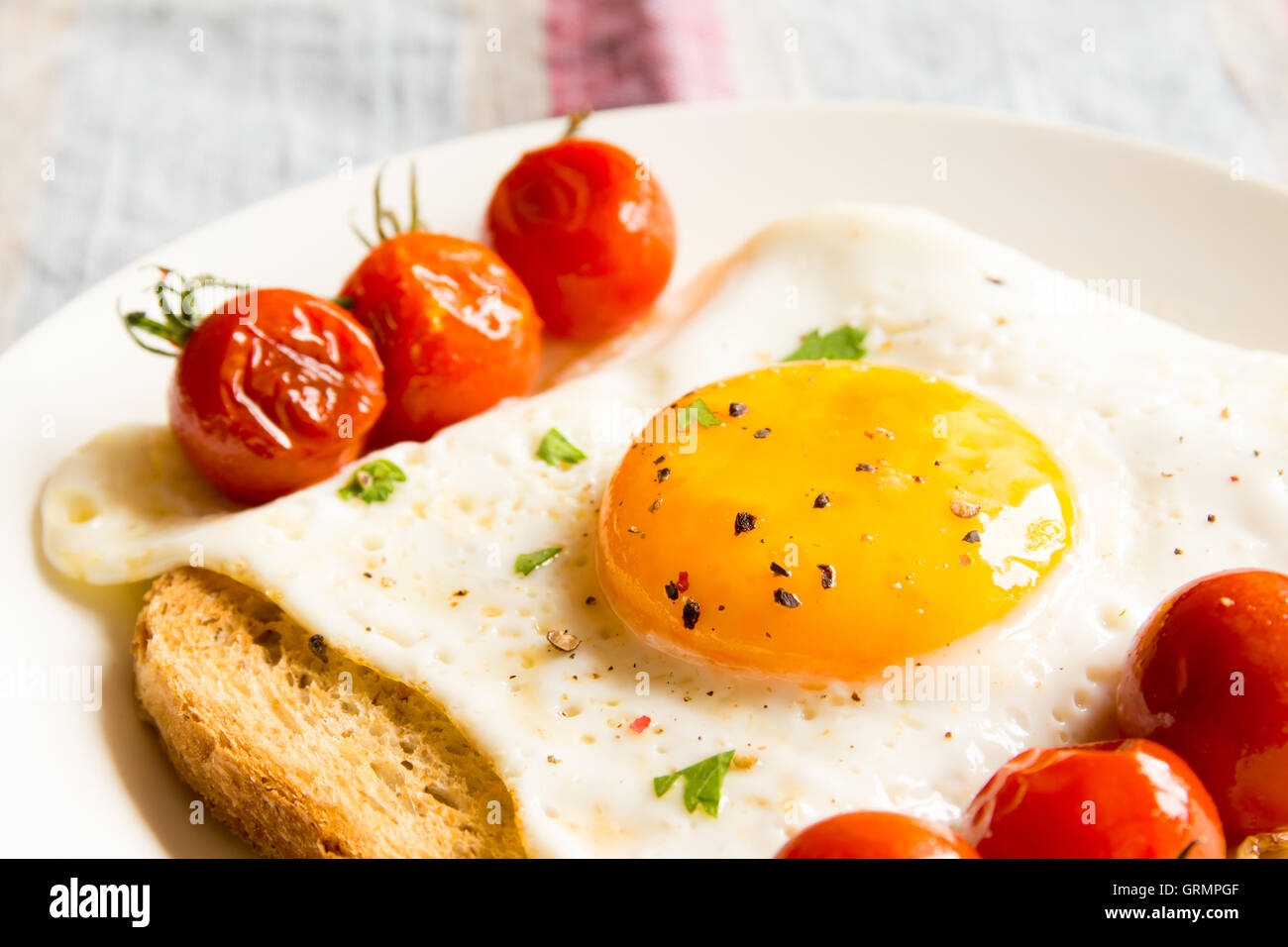 Fried egg on bread and fried tomatoes for breakfast on plate and rustic table Stock Photo