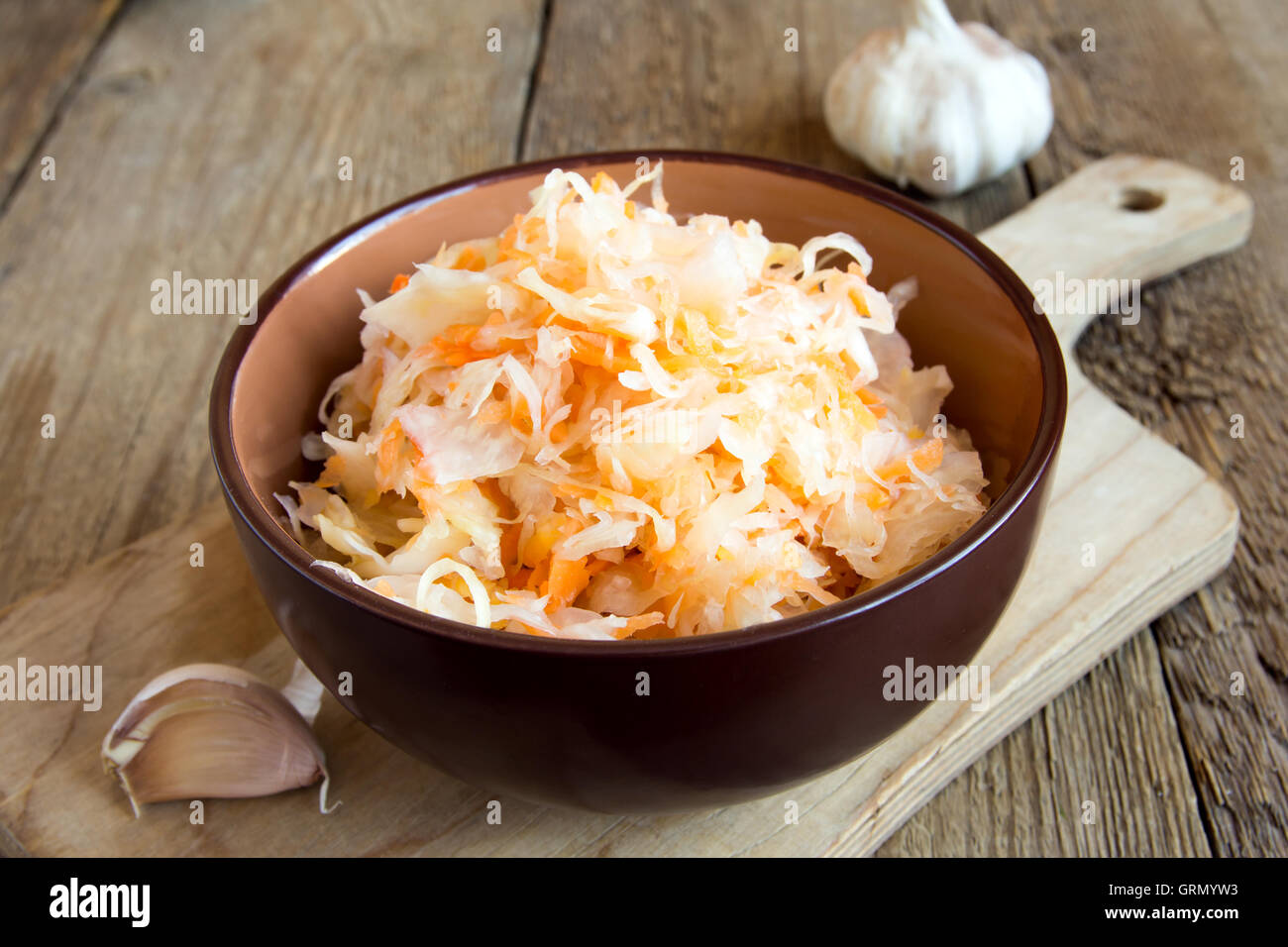Sauerkraut in ceramic bowl on rustic wooden table with garlic, traditional rustic winter food Stock Photo