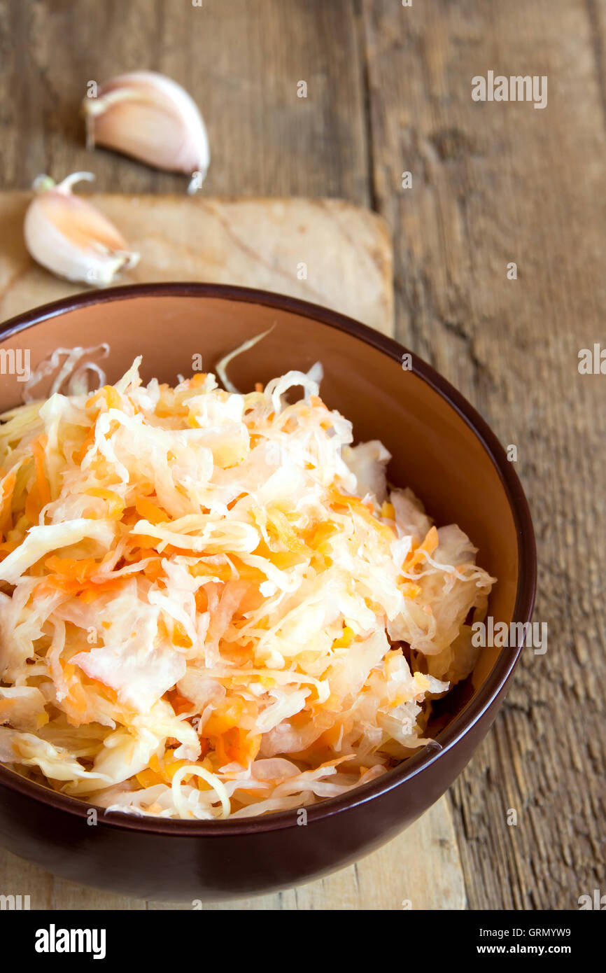 Sauerkraut in ceramic bowl on rustic wooden table with garlic, traditional rustic winter food Stock Photo