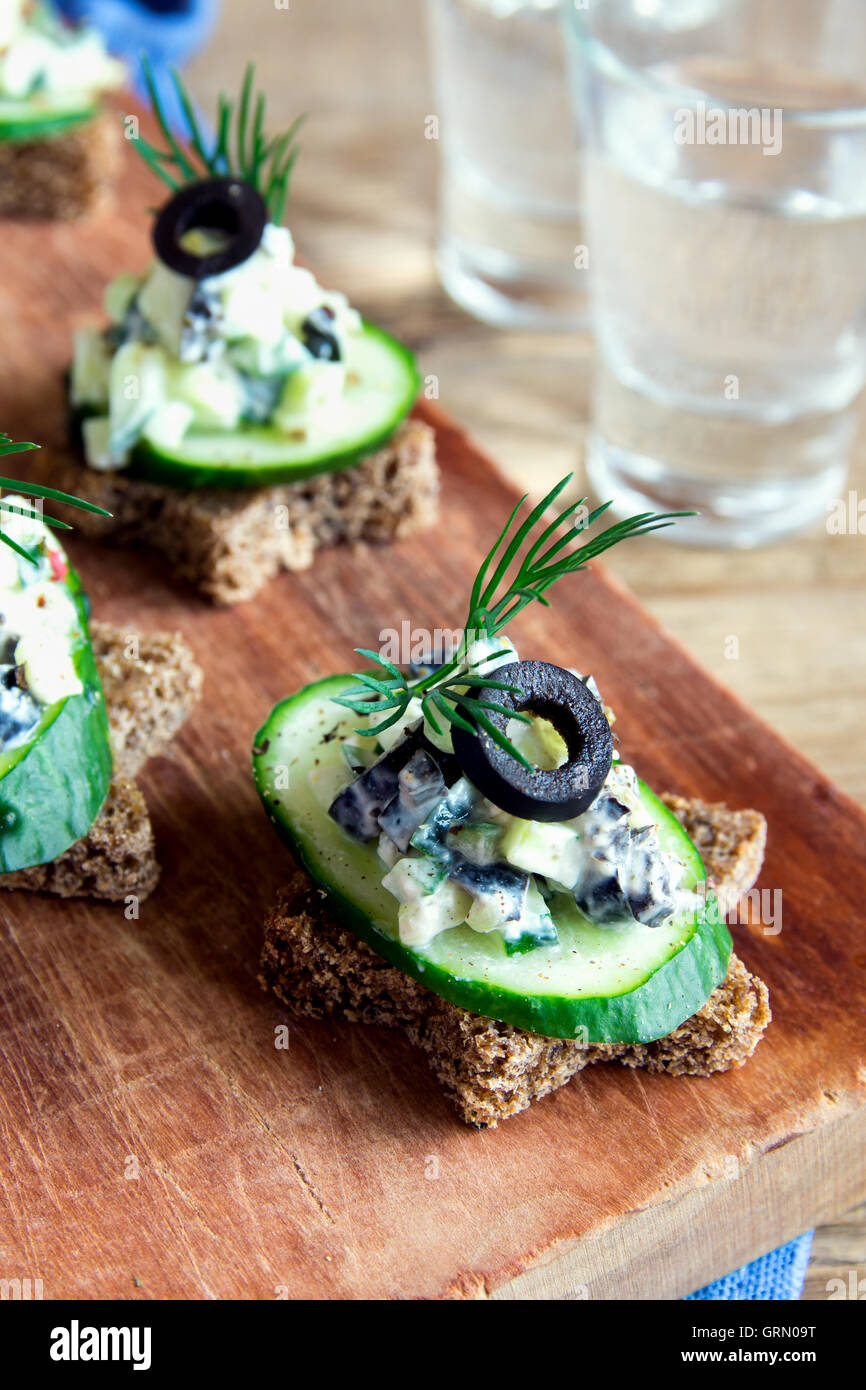 Mini sandwiches (snacks) with cucumber, olives and fish salad over ...