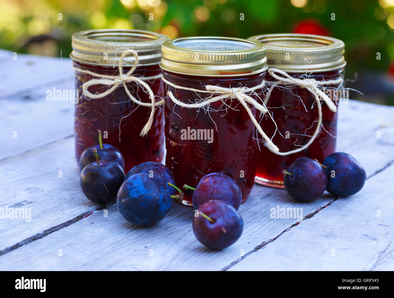 Bottles of homemade plum jam and some plums on an outside picnic table. Stock Photo