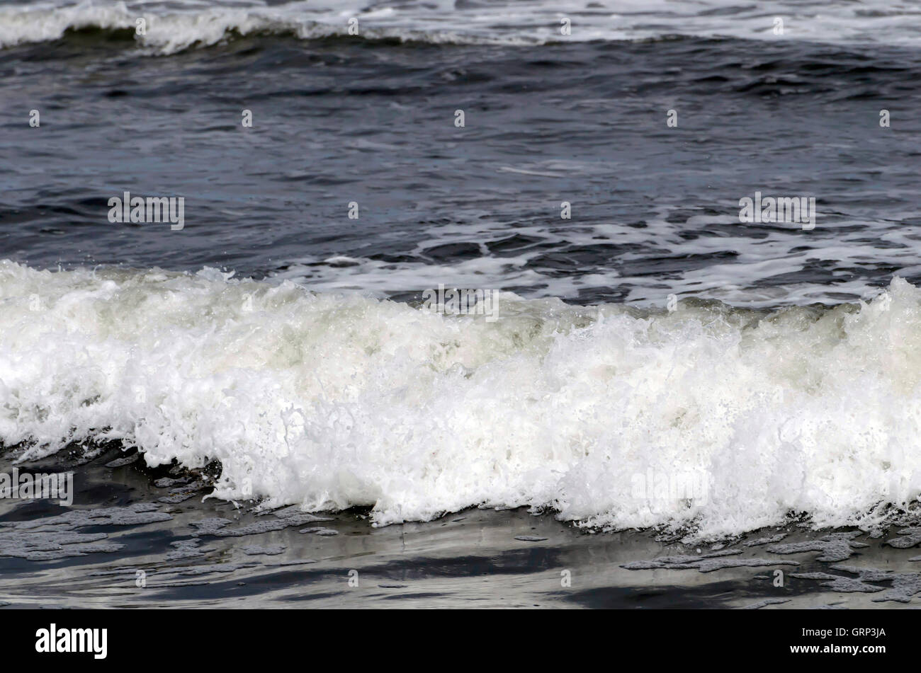 Waves breaking on a pebble-covered beach at Lindisfarne (Holy) Island in Northumberland, England. Stock Photo