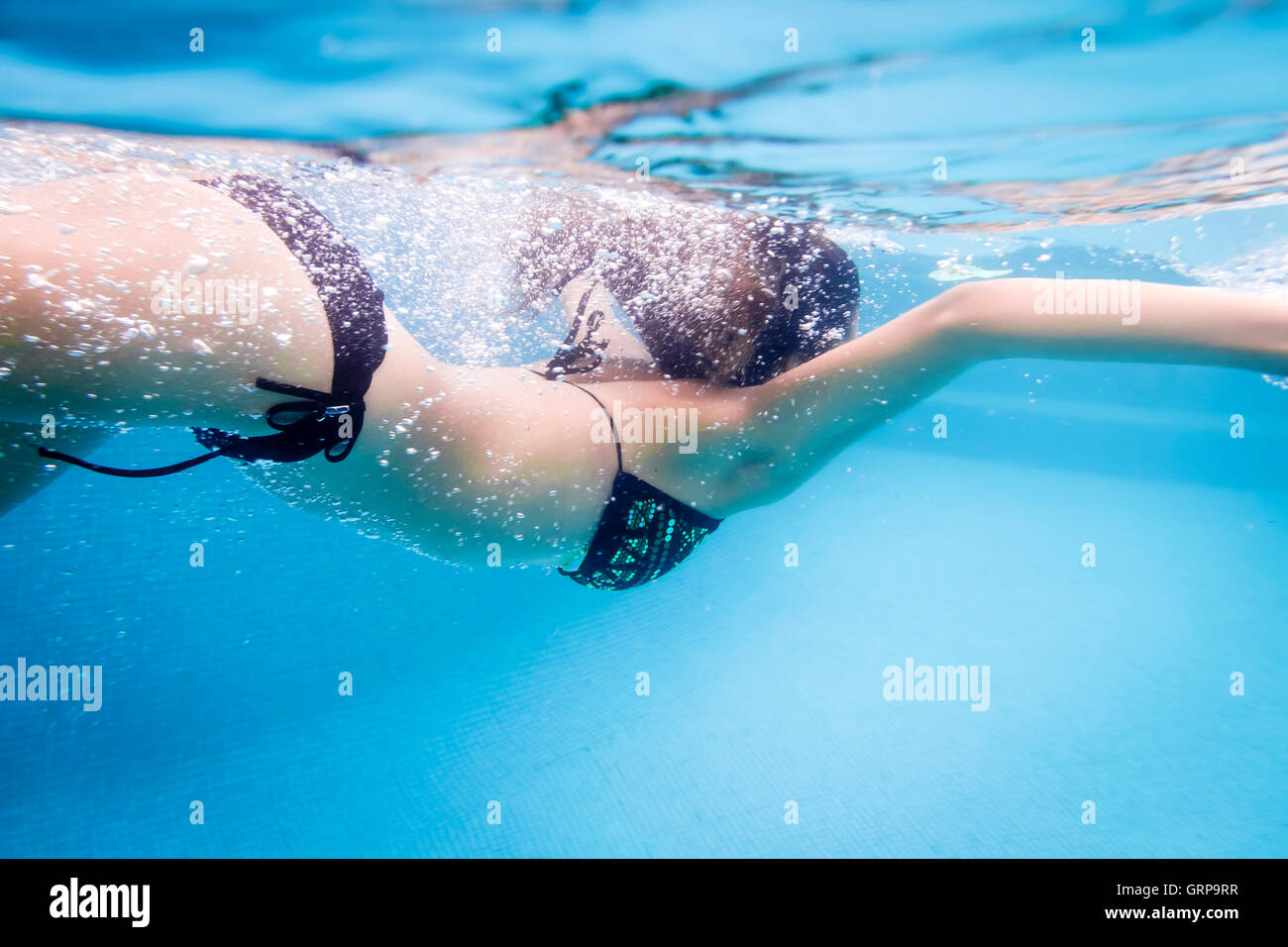Young woman swimming underwater with bubbles in swimming pool Stock Photo