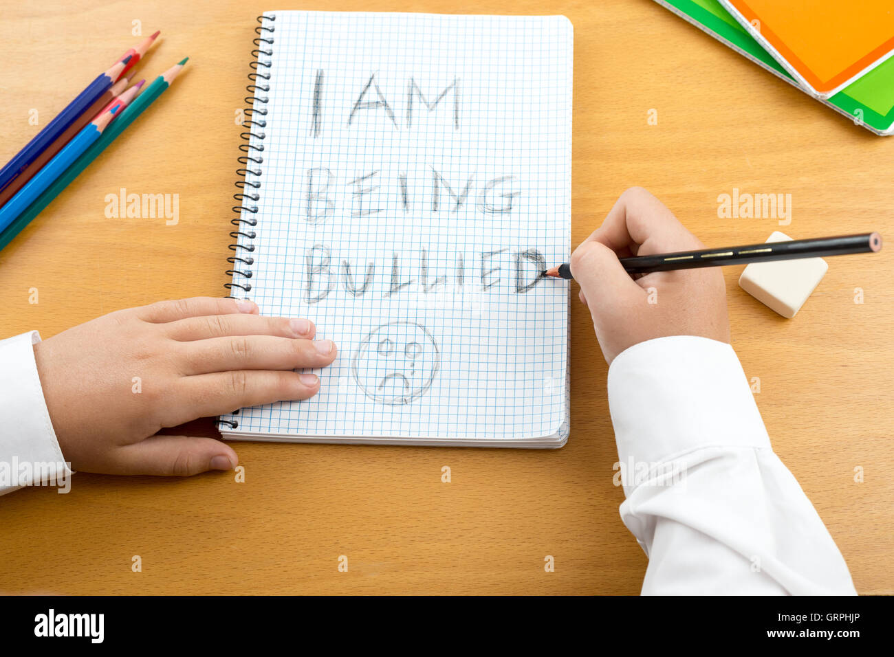 An image / poster covering the Social Issues of child abuse,  schoolchild in uniform at a desk asking for help by a written Stock Photo