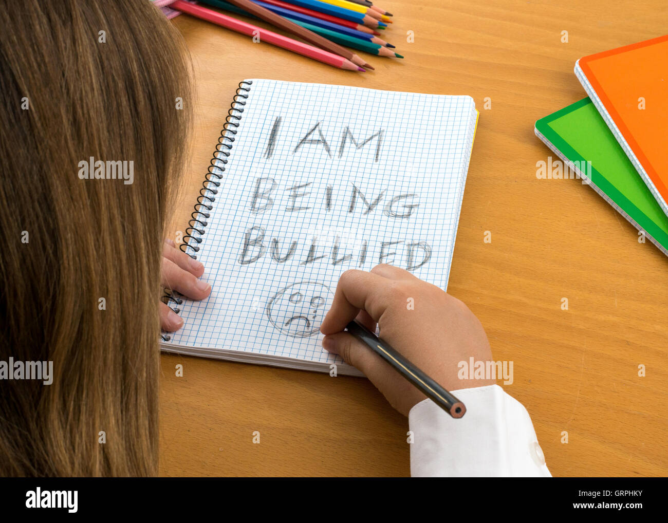 An Horizontal image / poster covering the Social Issues of child abuse,  schoolchild in uniform at a desk asking for help Stock Photo