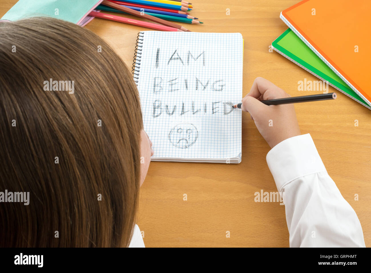 An Horizontal image / poster covering the Social Issues of child abuse,  schoolchild in uniform at a desk asking for help Stock Photo