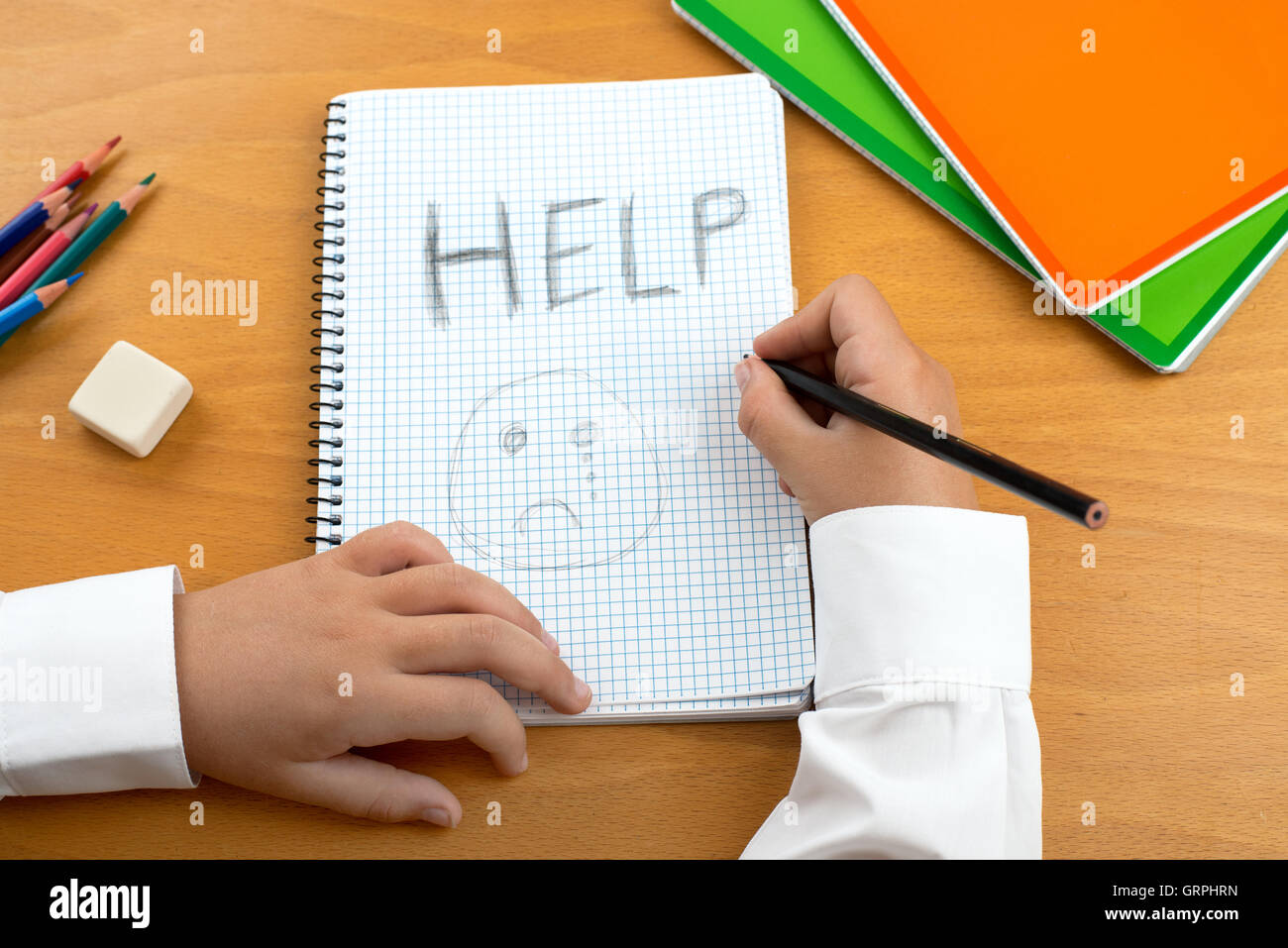 An image /poster covering the Social Issues of child abuse, schoolchild in uniform at a desk asking for help by a written Stock Photo