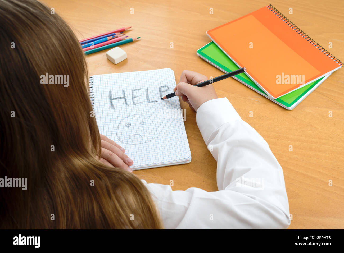 A Horizontal image /poster covering the Social Issues of child abuse, by a schoolchild sat at a desk asking for help Stock Photo