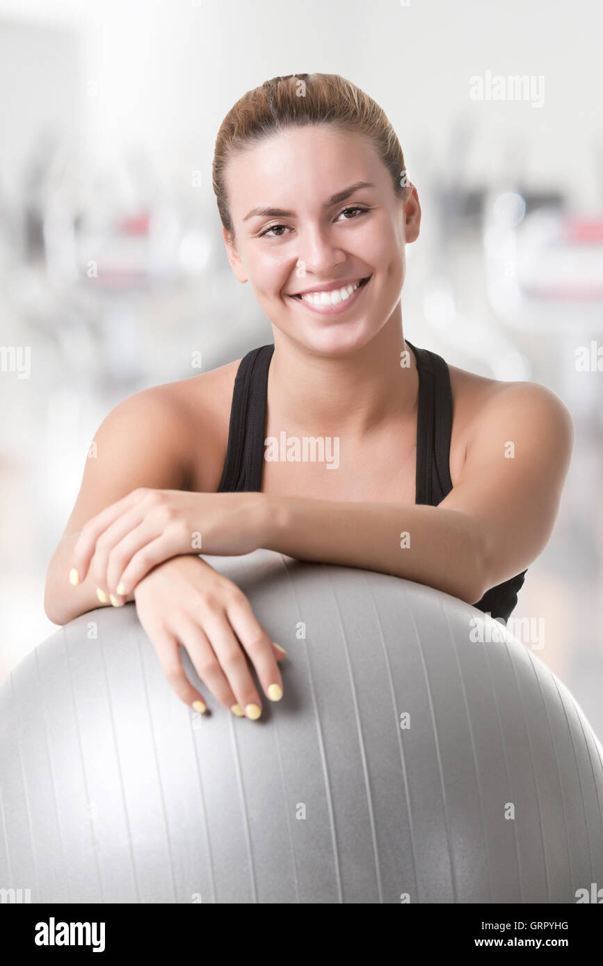 Fit woman sitting and holding a pilates ball on the floor, in a gym Stock Photo