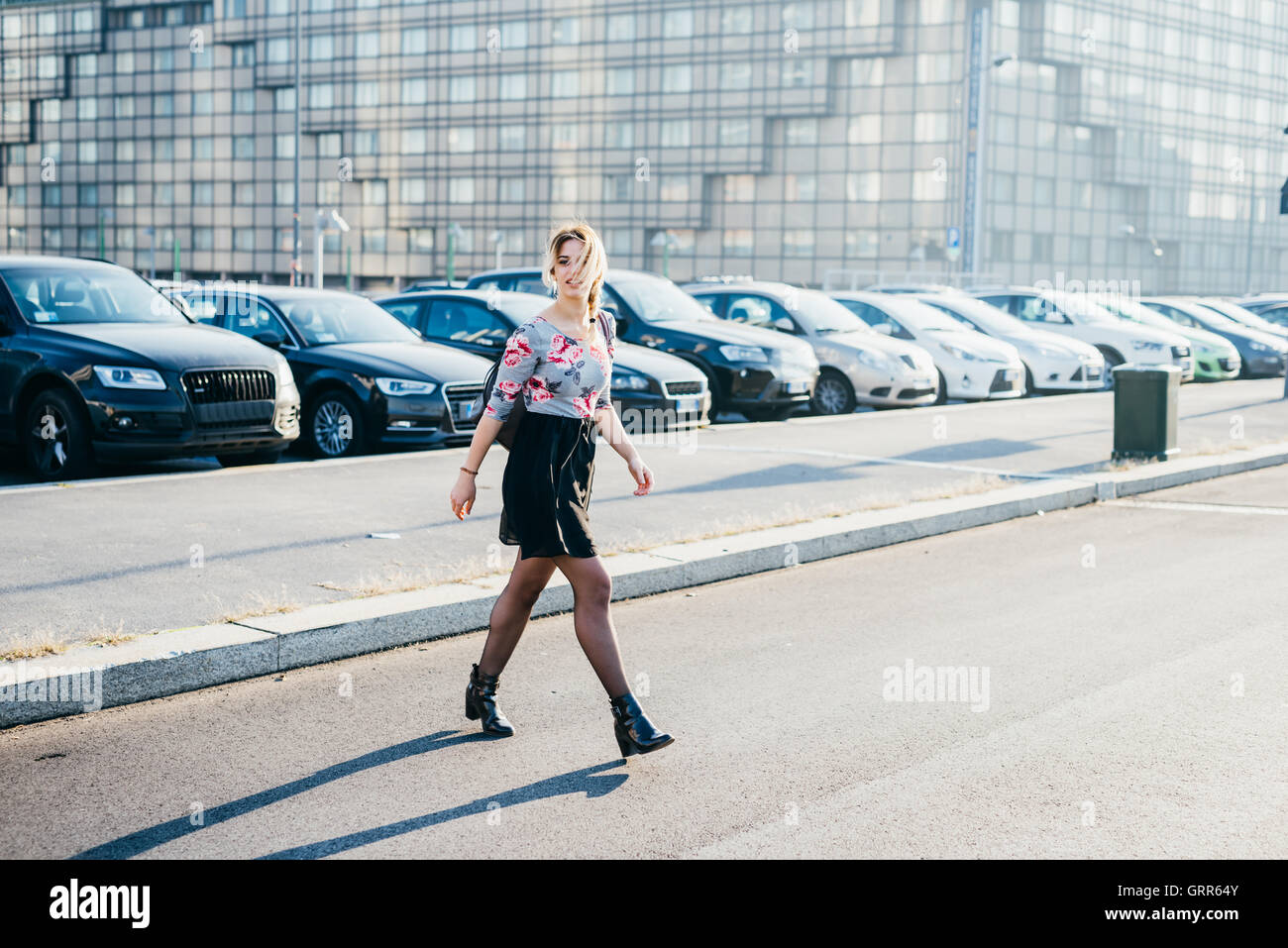 young beautiful blonde woman  crossing the street outdoor in the city listening music with earphones - music, technology, relaxi Stock Photo