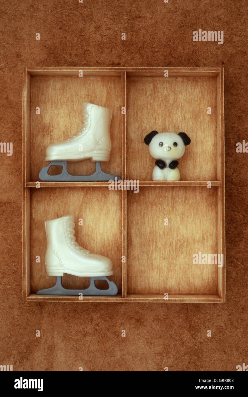 Small wooden compartments containing vintage plastic models of panda and doll ice-skating boots Stock Photo