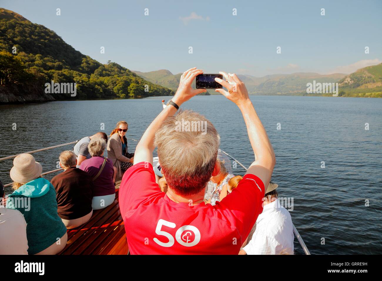 Tourists enjoying a cruise  and taking photographs with a smart phone aboard the bow of Ullswater Steamers. Ullswater, Penrith. Stock Photo