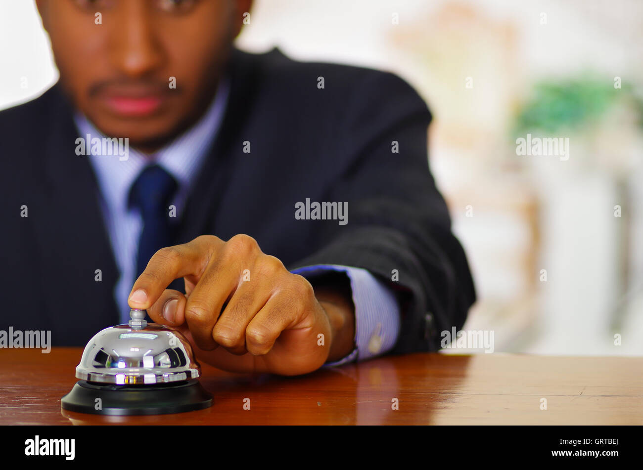 Man wearing elegant blue suit pressing desk bell at hotel reception