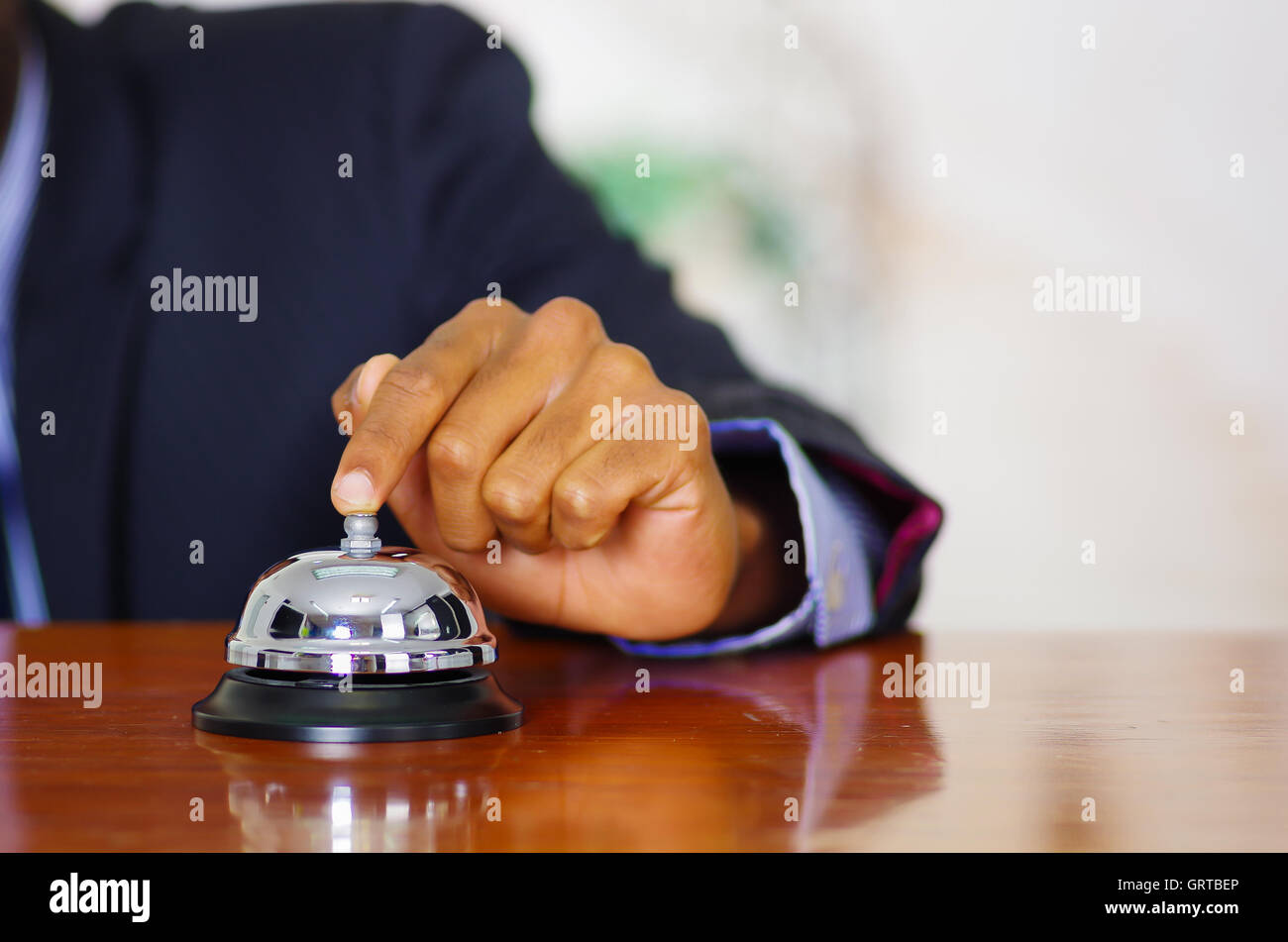 Closeup arm of man wearing blue suit pressing desk bell at hotel
