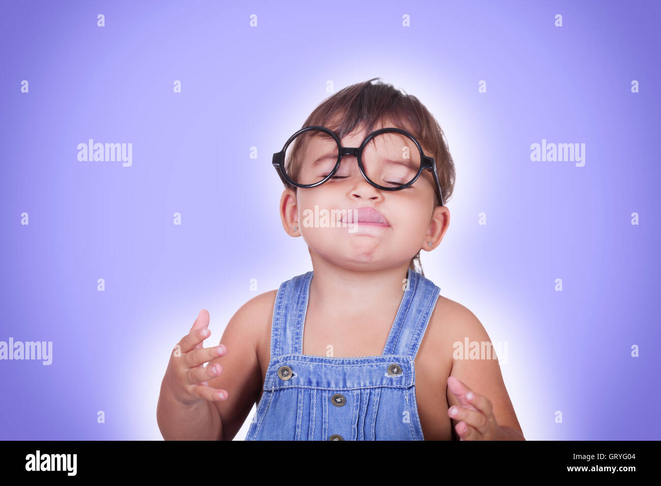 Studio portrait of cute kid in glasses imagines some yummy food with eyes closed licking lips.Isolate.Blue background. Stock Photo