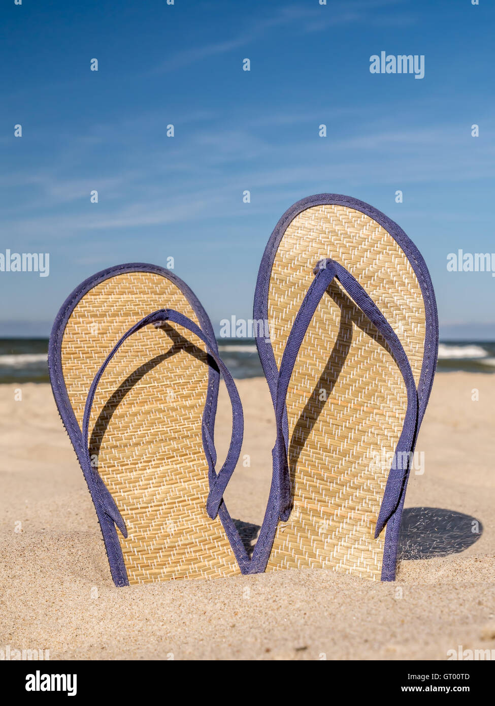 Pair of straw flip-flops stuck into beach sand over blue sky Stock Photo