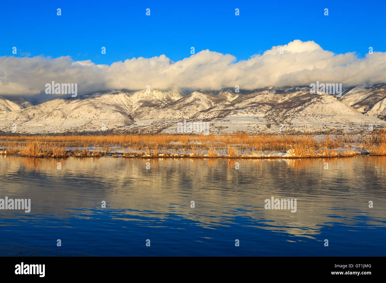 The clouds hug the tops of the Wasatch Mountains and reflect in the open water at Farmington Bay Waterfowl Management Area USA Stock Photo