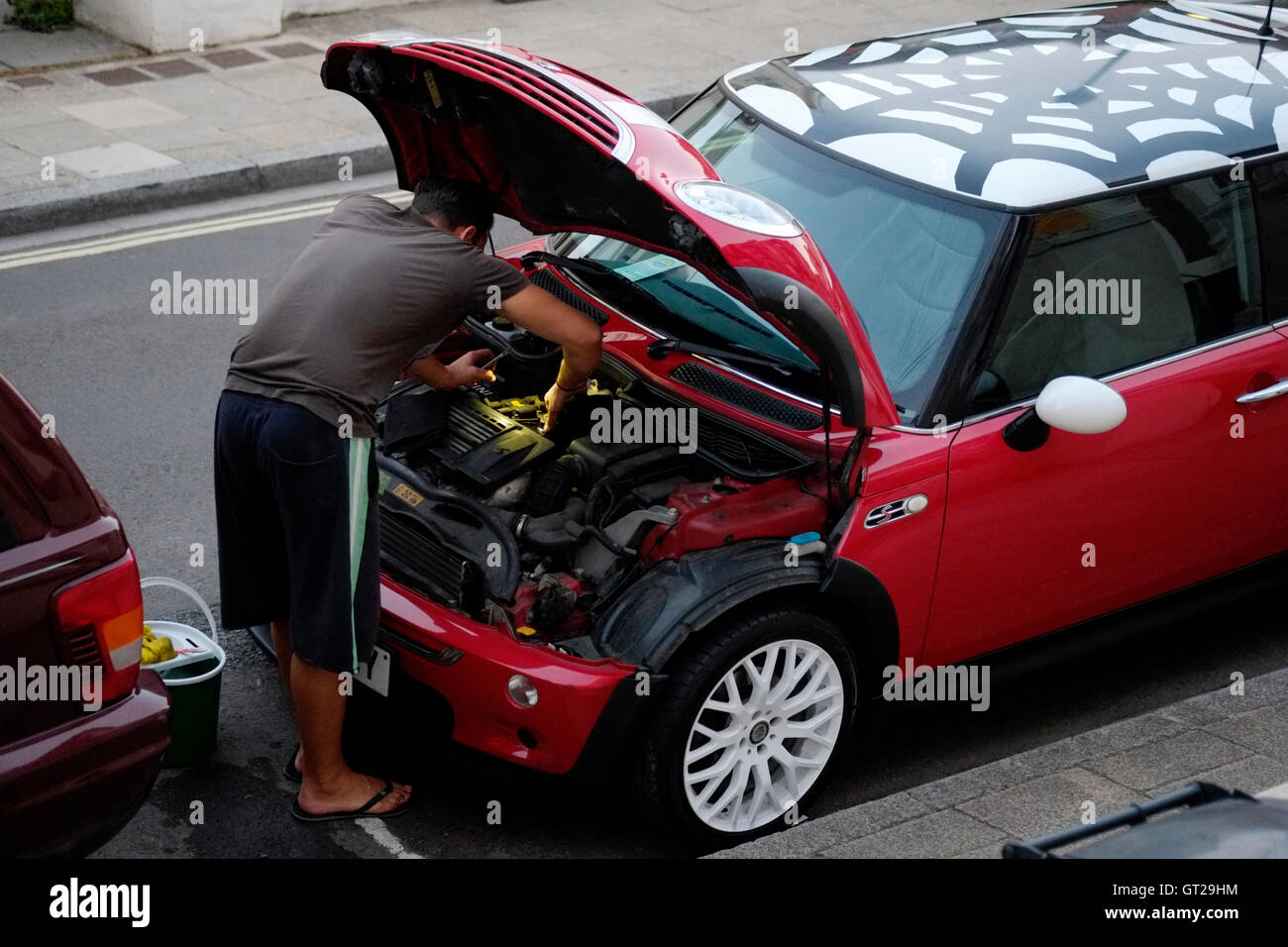 man cleaning car engine bay at dusk using light from his smart phone england uk Stock Photo