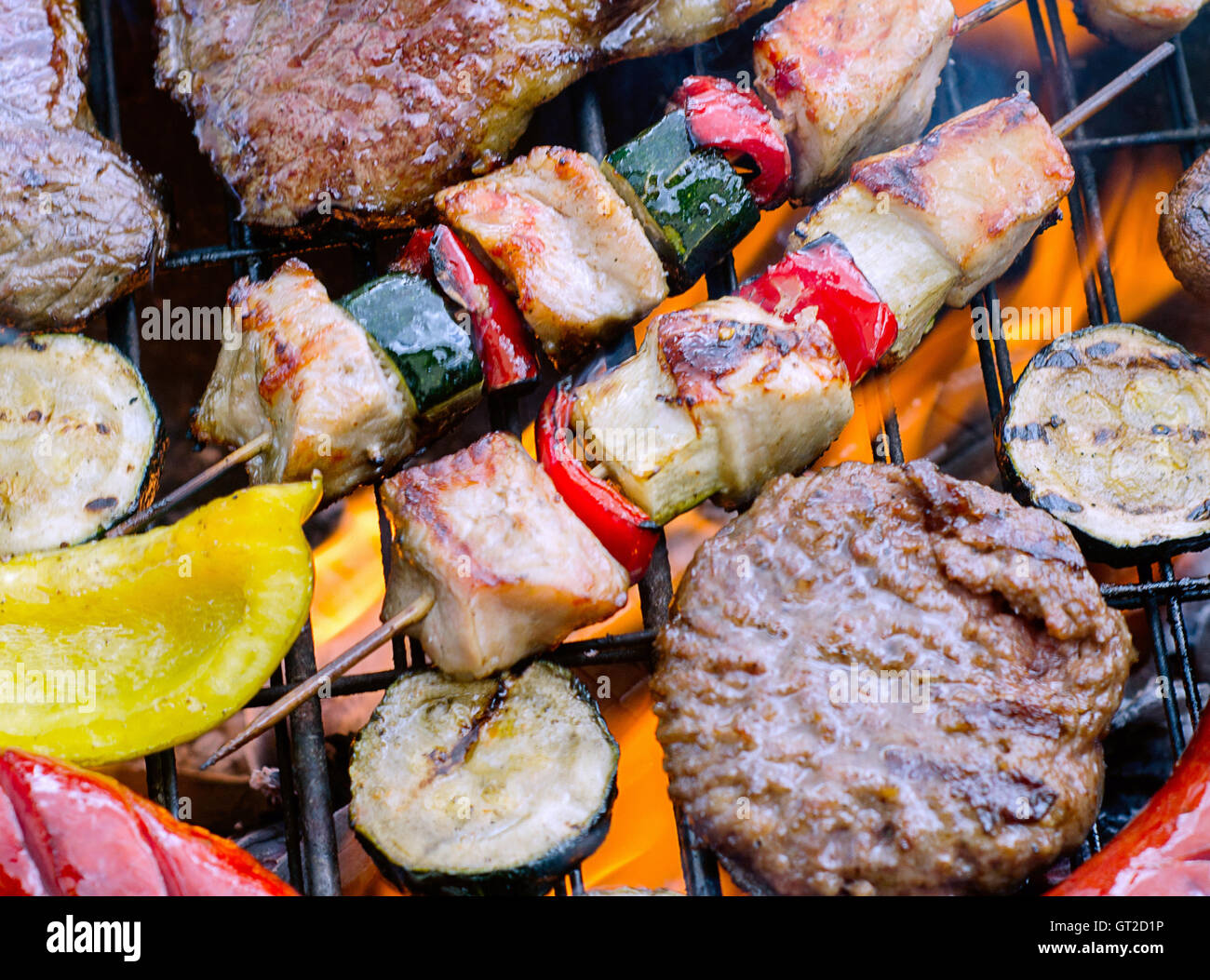 Assorted meat with vegetables cooking on grill with flames. Stock Photo