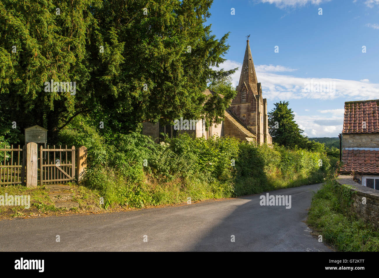 Sunny, evening view along a quiet country lane, passing the old church in pretty Rievaulx Village, North Yorkshire, England. Stock Photo
